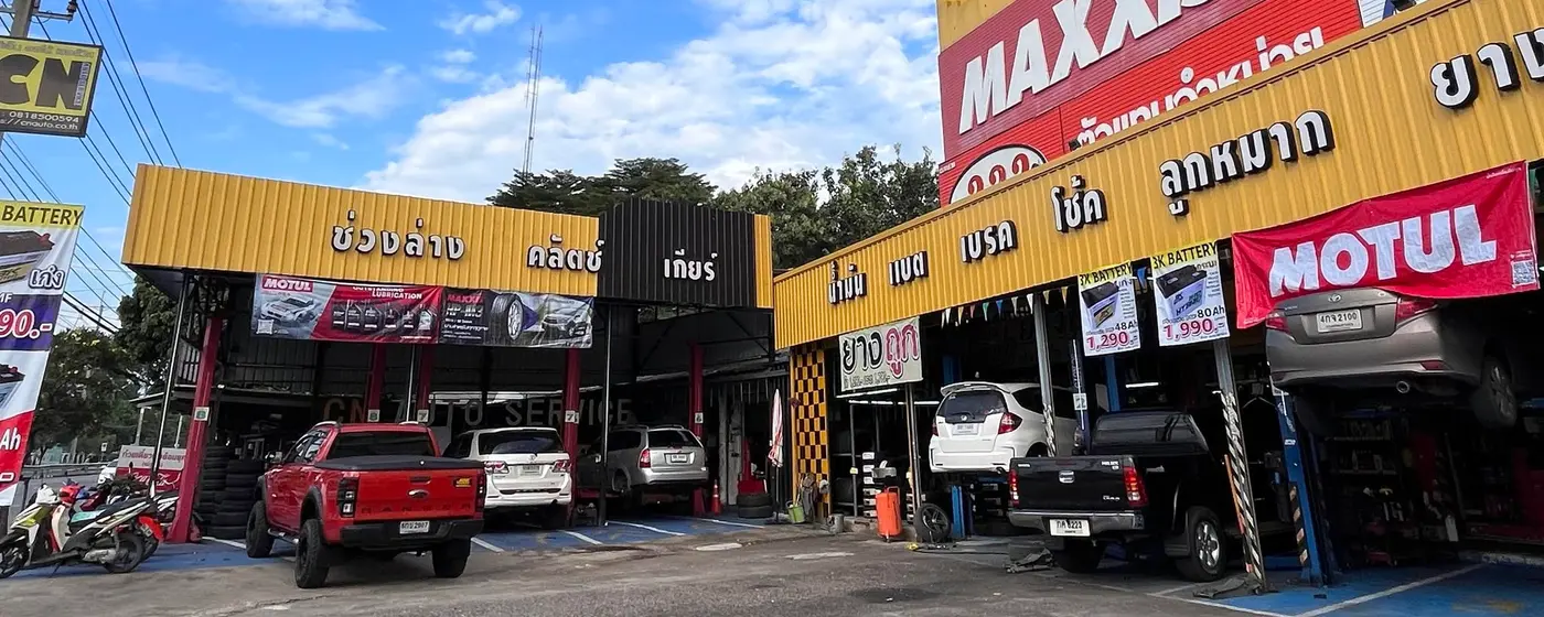 หน้าร้าน CN Auto Service มีป้ายบริการช่วงล่าง คลัตช์ เกียร์ น้ำมัน แบต เบรค โช้ค ลูกหมาก และรถหลายคันจอดอยู่ในช่องบริการ